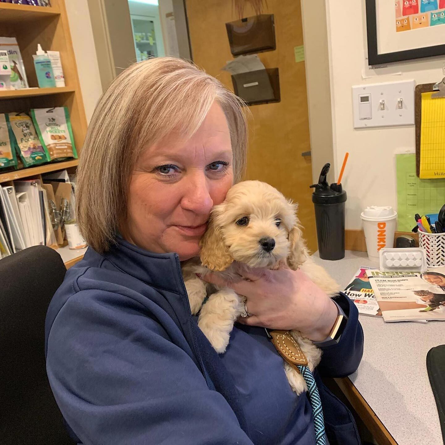 female staff member smiling and holding up small golden retriever puppy to face